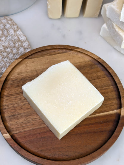 Square soap on a round wooden dish with some soaps noticeable in the background