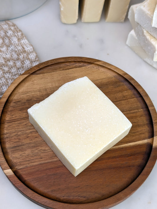 Square soap on a round wooden dish with some soaps noticeable in the background