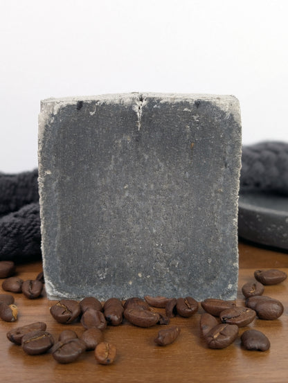 Square bar of charcoal coffee soap with coffee beans on a wooden surface