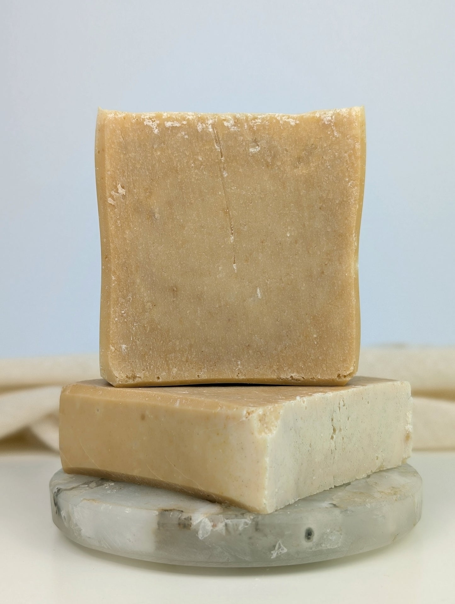 Two bars of soap stacked on a clear stone surface with a white background