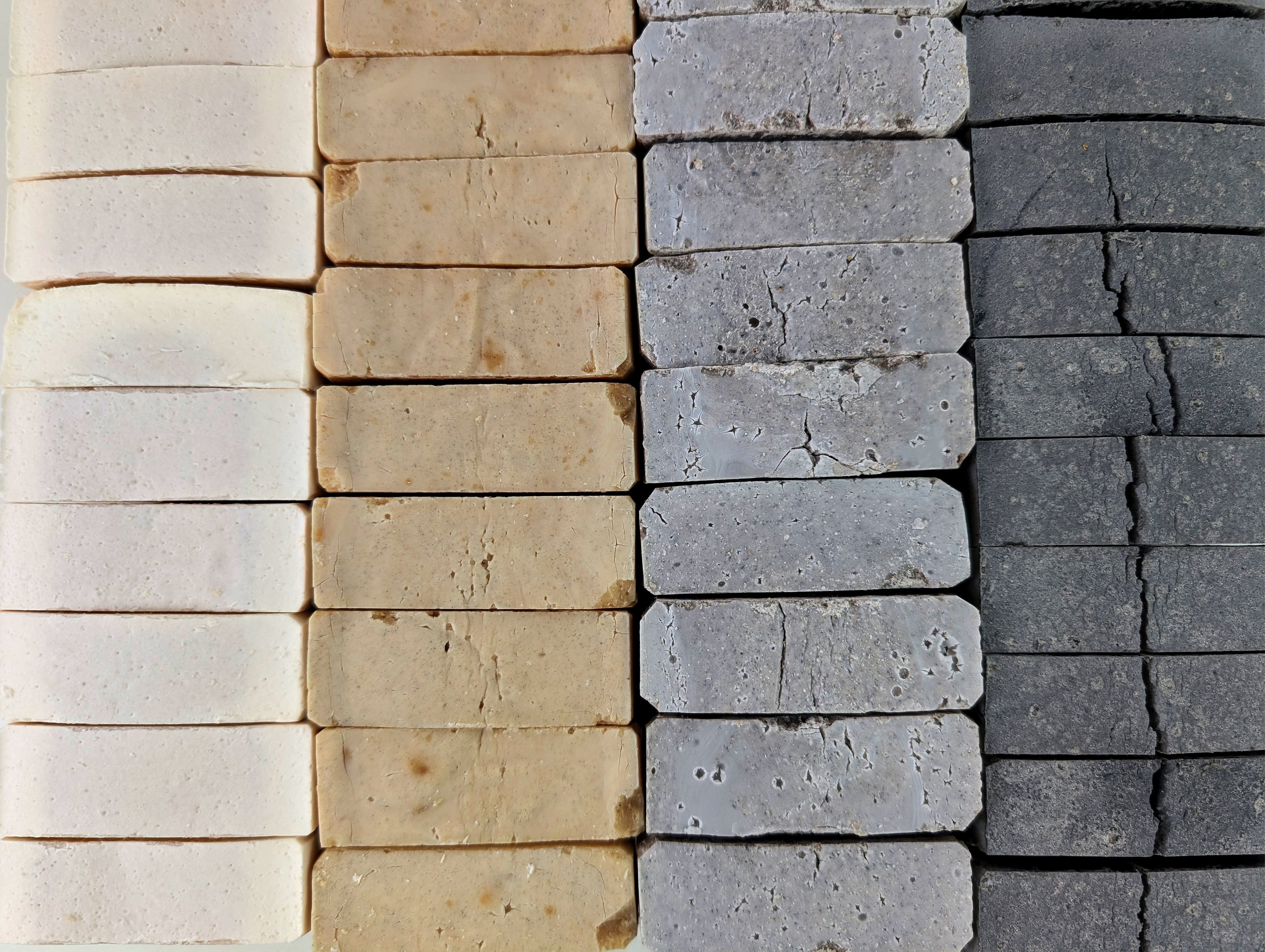 Top down view of handmade soaps lined up in tight rows in various colors including beige, gray, and black.